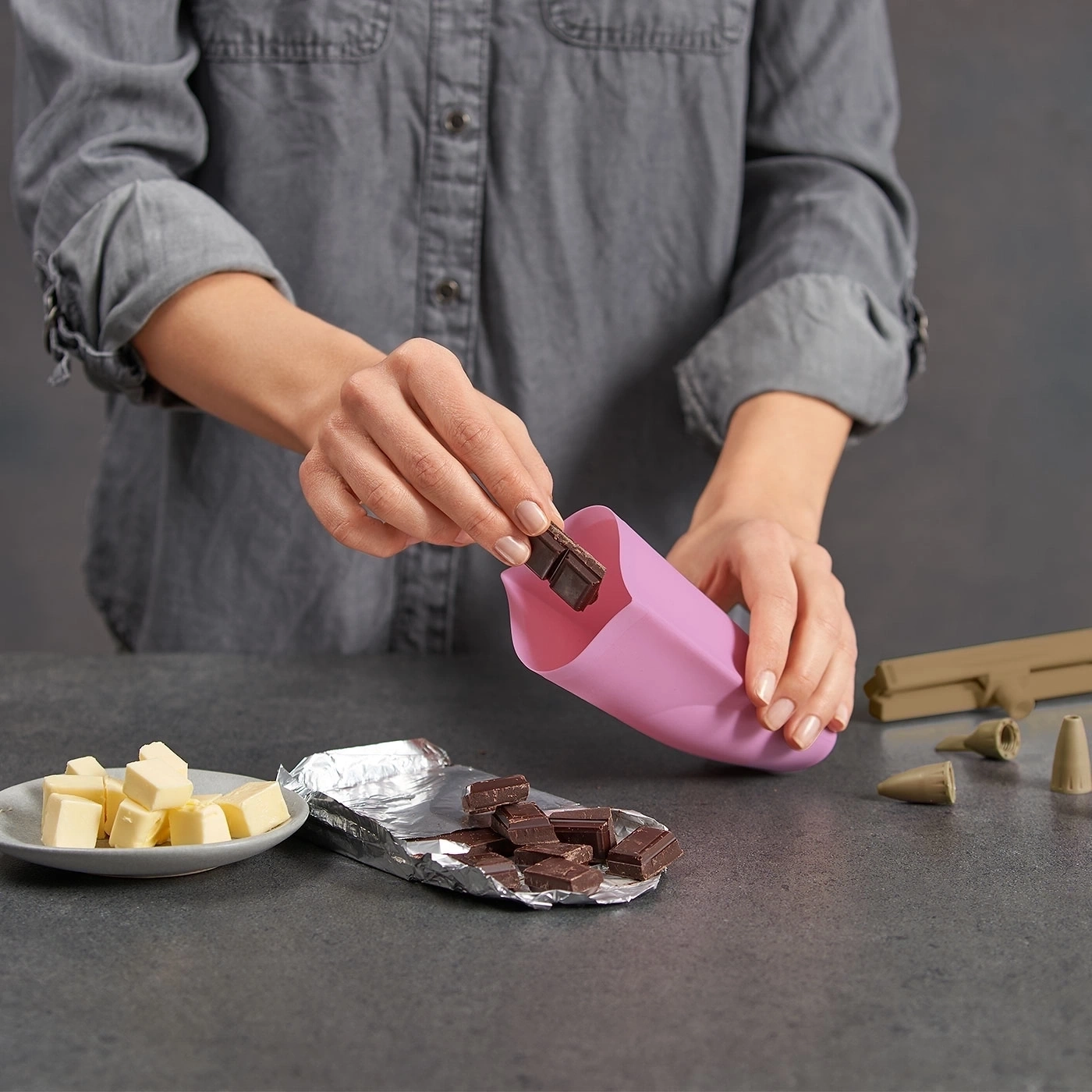 Person legt Schokoladenstücke in einen rosa Beutel. Butter und Schokoladenstücke auf dem Tisch.