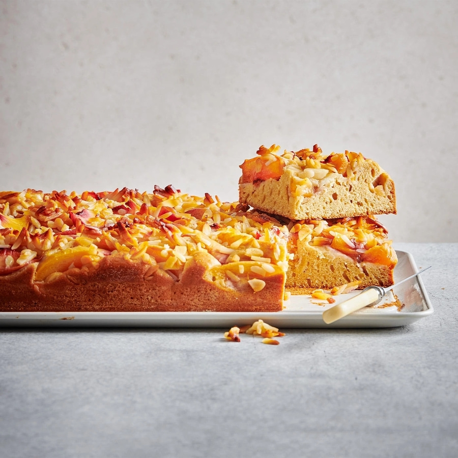 Kuchen mit Mandeln und Pfirsichen auf einem Teller, angeschnitten
