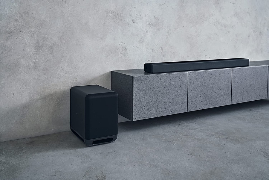 Schwarzer Subwoofer und Soundbar auf grauem Schrank vor grauer Wand
