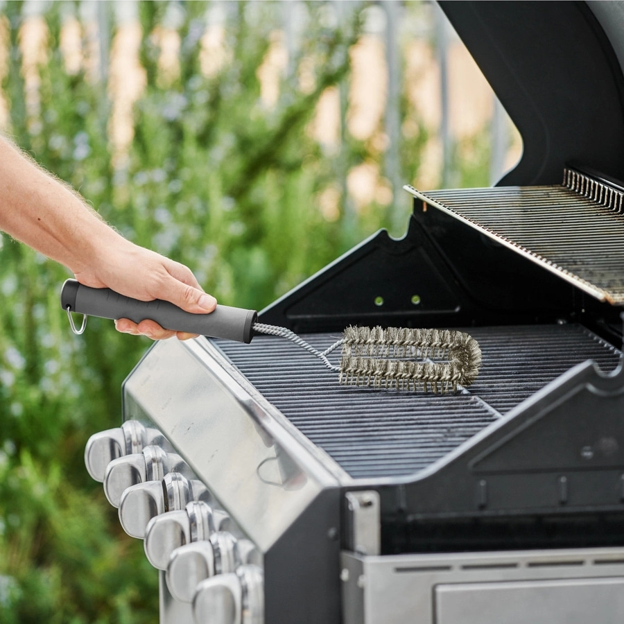 Person reinigt Grillrost mit Bürste im Freien, Nahaufnahme.