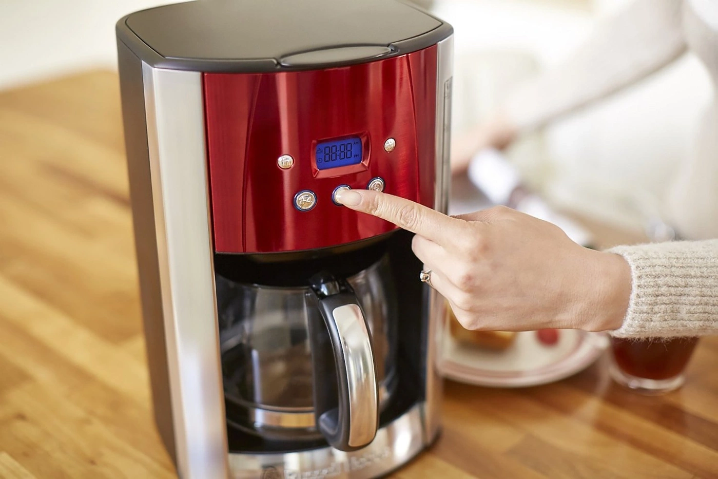 Kaffeemaschine mit roter Front, Hand drückt Knopf, Digitalanzeige, Tisch
