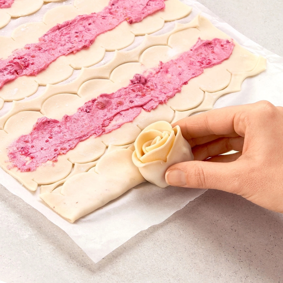 Nahaufnahme von Gebäck mit rosa Creme und einer Hand, die eine Rose formt.