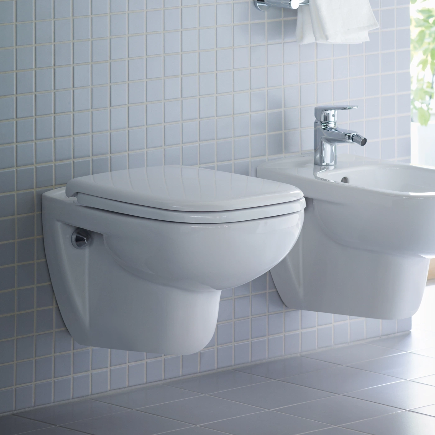 Ein modernes Badezimmer mit Wandfliesen, einem Wand-WC und einem Bidet mit Chromarmatur.