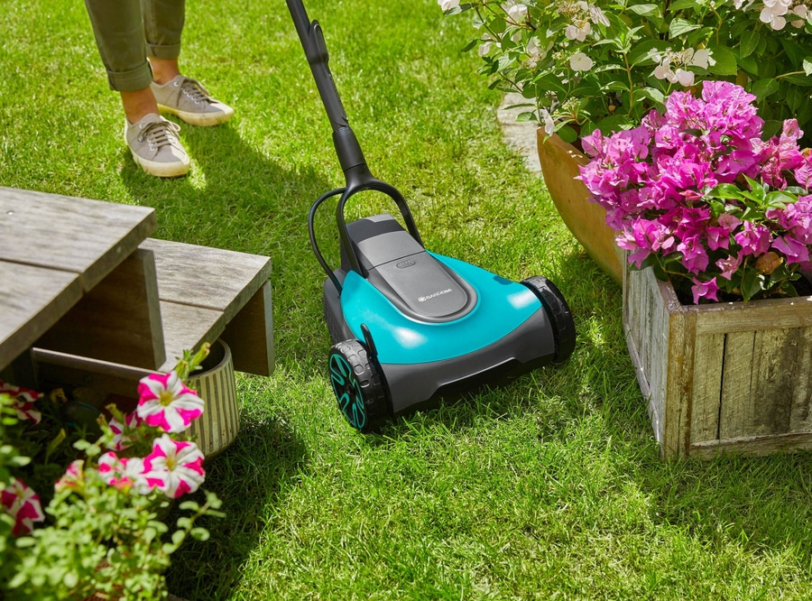 Rasenmäher im Garten neben Blumen und Holzbank