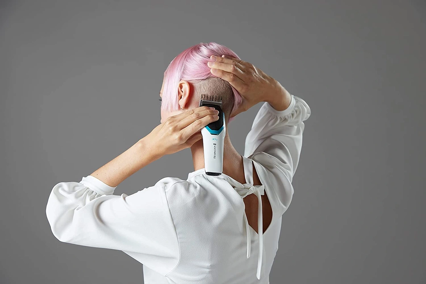 Person schneidet sich mit einem Rasierer die Haare, rosa Haare, weißes Hemd