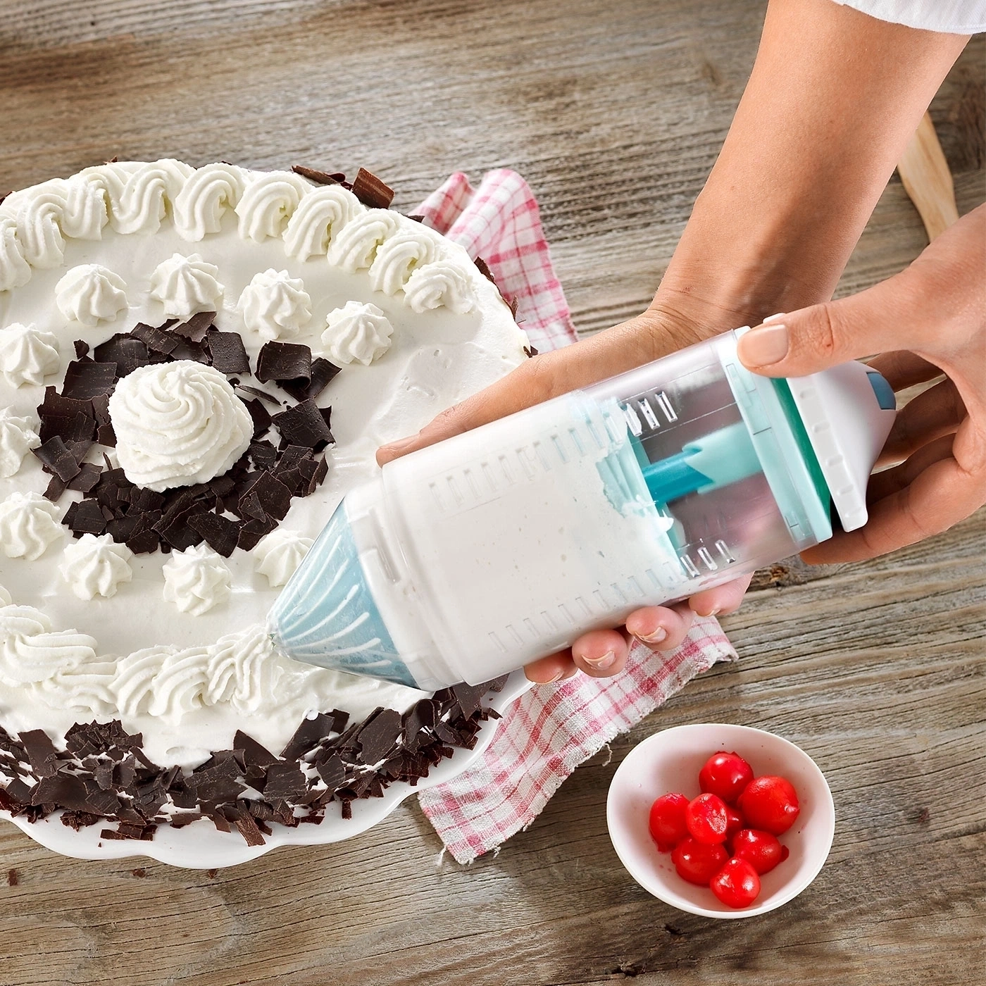 Kuchen wird mit Sahne verziert, Kirschen in einer Schale, Holzuntergrund.