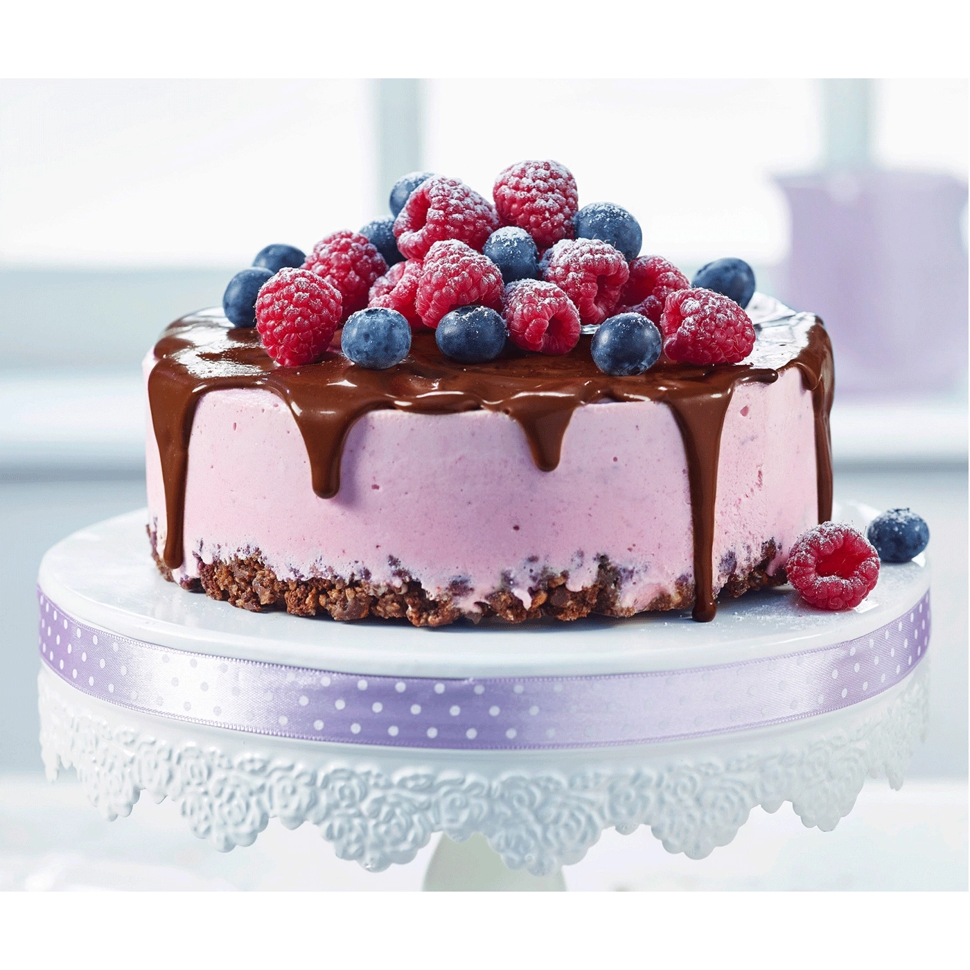 Kuchen mit Schokoladenglasur, Himbeeren und Blaubeeren auf einem Tortenständer