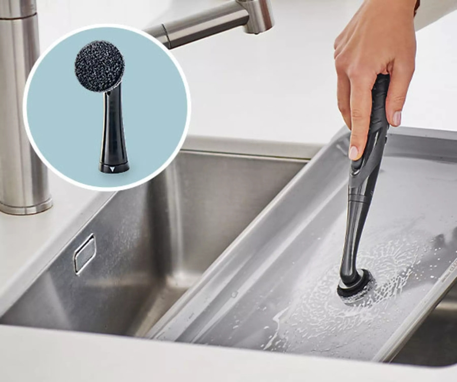 Eine Person reinigt eine Metallwanne mit einer schwarzen Bürste in einem Waschbecken.