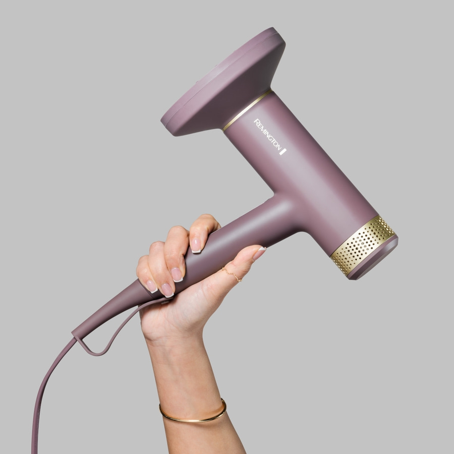 Hand hält einen lila Haartrockner mit goldenen Akzenten und dem Markennamen Remington.