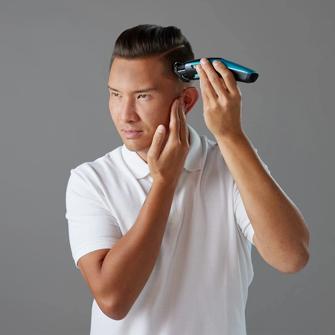 Mann schneidet sich mit einem Rasierer die Haare, grauer Hintergrund, weißes Hemd