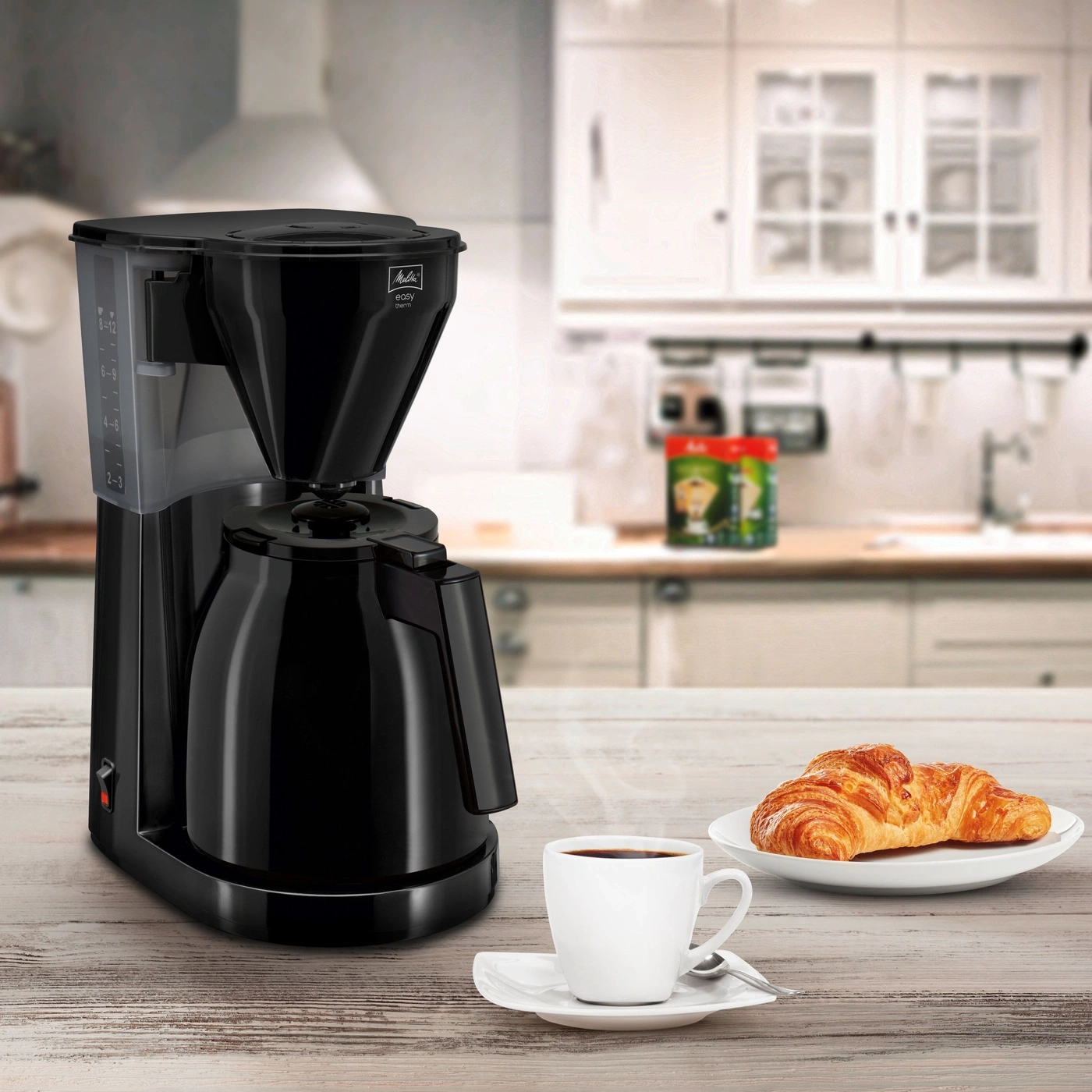 Kaffeemaschine mit Tasse Kaffee und Croissant auf einem Holztisch in der Küche