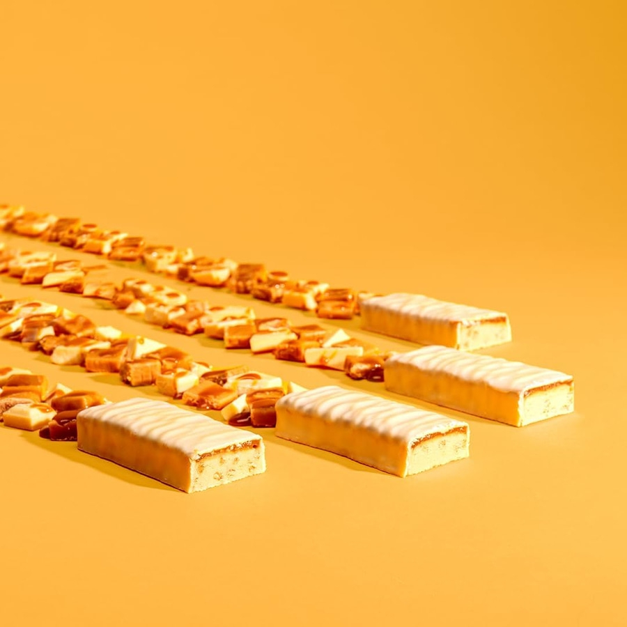 Mehrere Schokoriegel mit weißer Glasur und Karamellfüllung auf orangefarbenem Hintergrund.