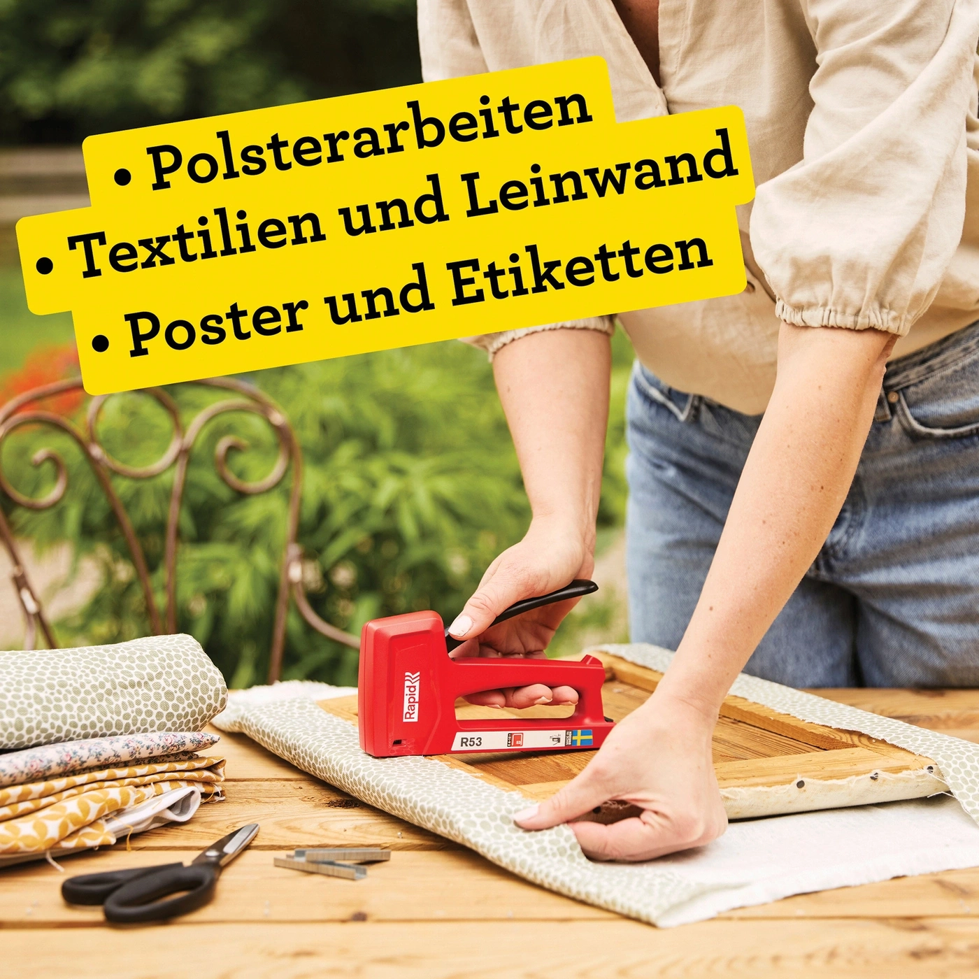 Person polstert mit rotem Tacker ein Holzobjekt mit Stoff.