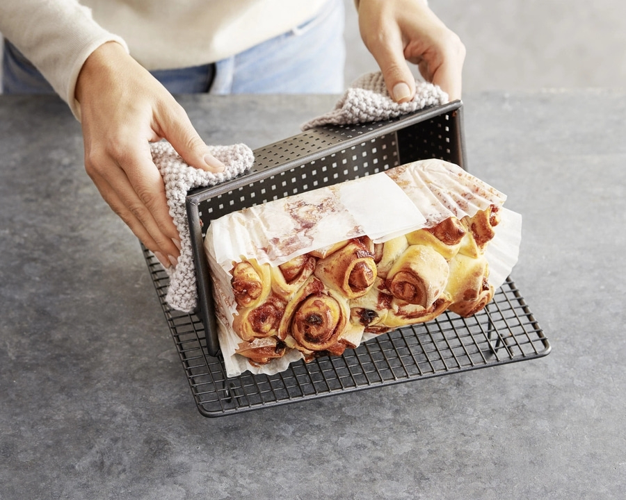 Person hält Backform mit Gebäck, das auf einem Rost abgekühlt wird.