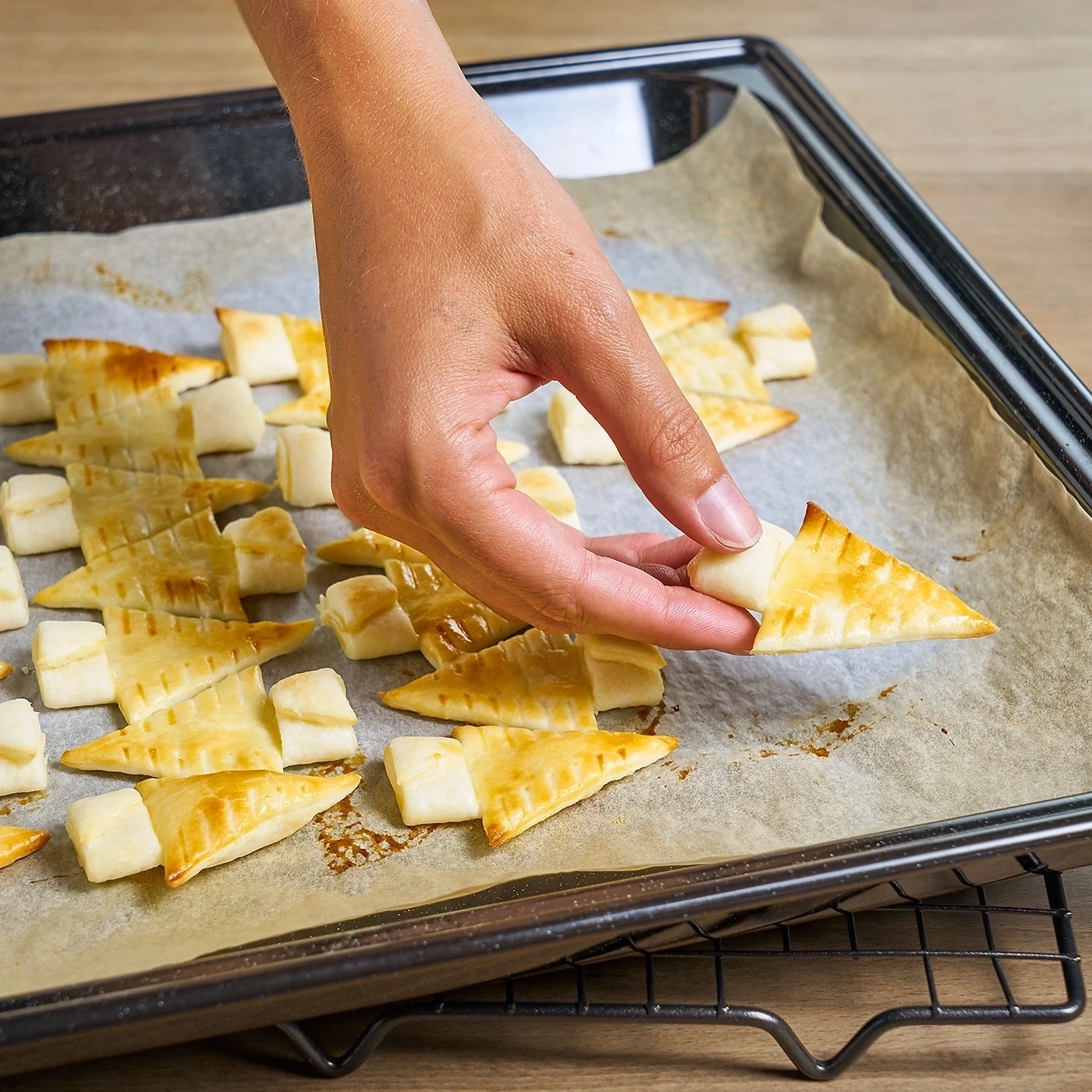 Hand hält Gebäck auf Backblech, das mit Backpapier ausgelegt ist.