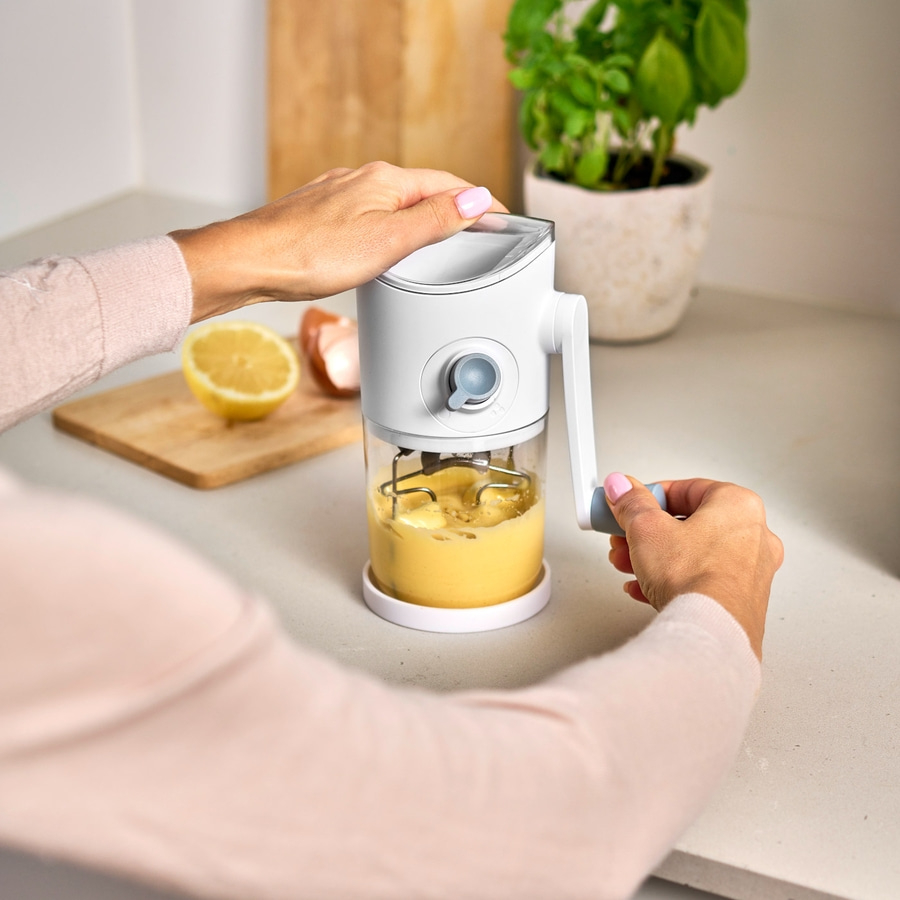 Person macht Mayonnaise mit einem Küchengerät, Zitrone und Pflanze im Hintergrund.