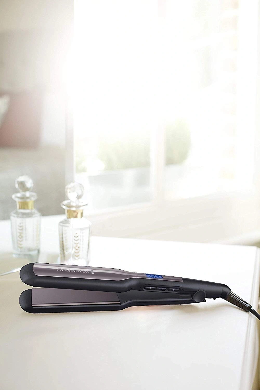 Haarglätter von Remington auf weißer Oberfläche mit Flaschen im Hintergrund
