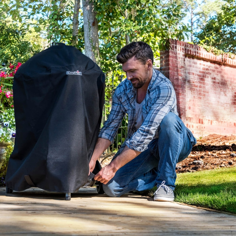 Mann kniet vor Grill, der mit einer schwarzen Abdeckung bedeckt ist, im Garten.