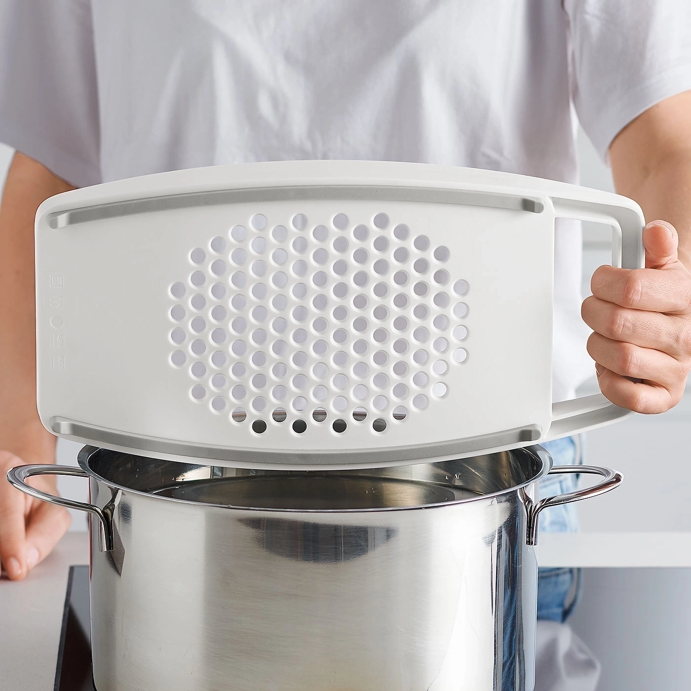 Person hält weißen Küchensieb über Topf mit Wasser. Kochen in der Küche.