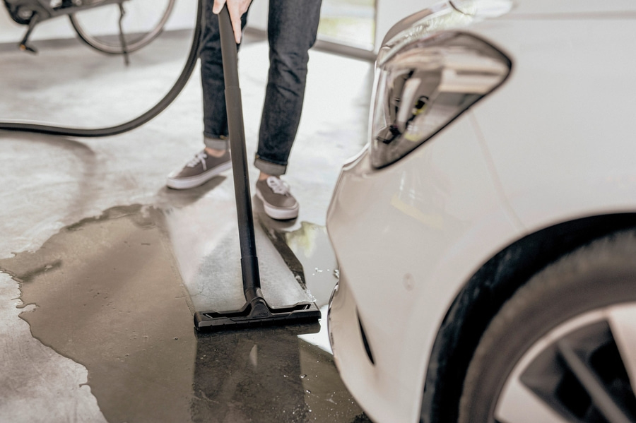 Person saugt Wasser mit einem Staubsauger in der Nähe eines Autos auf