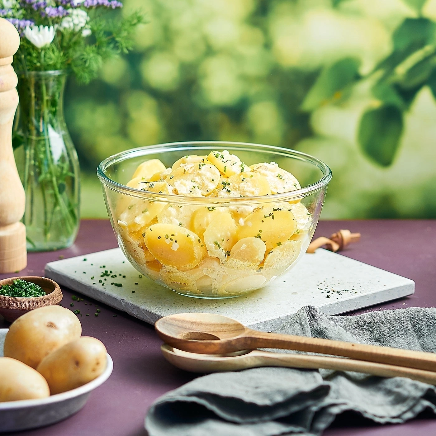 Kartoffelsalat in einer Glasschüssel mit Kräutern und Holzlöffeln auf einem Tisch