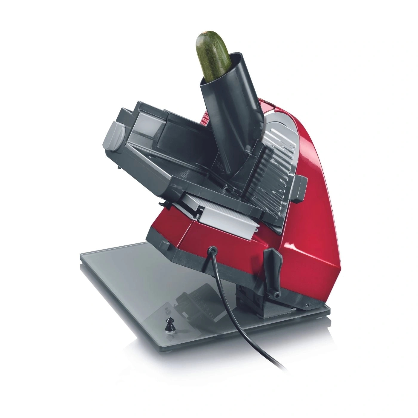 Rote elektrische Gemüseschneidemaschine mit Zucchini, die auf weißem Hintergrund steht.