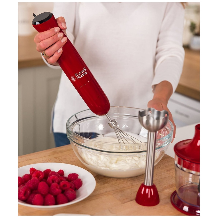 Person rührt Sahne mit einem roten Stabmixer, daneben Himbeeren.