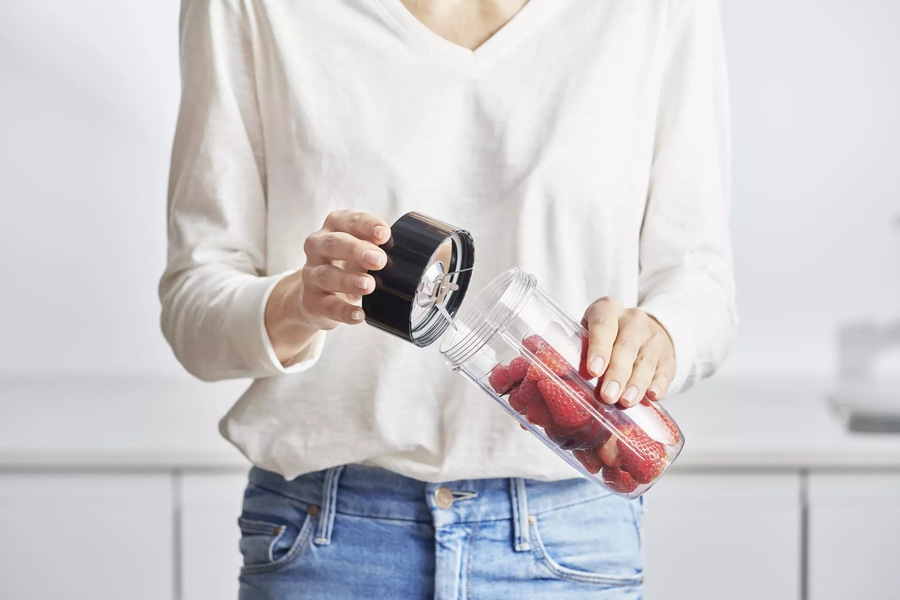 Person hält Mixer mit Erdbeeren, bereit für die Zubereitung eines Smoothies.