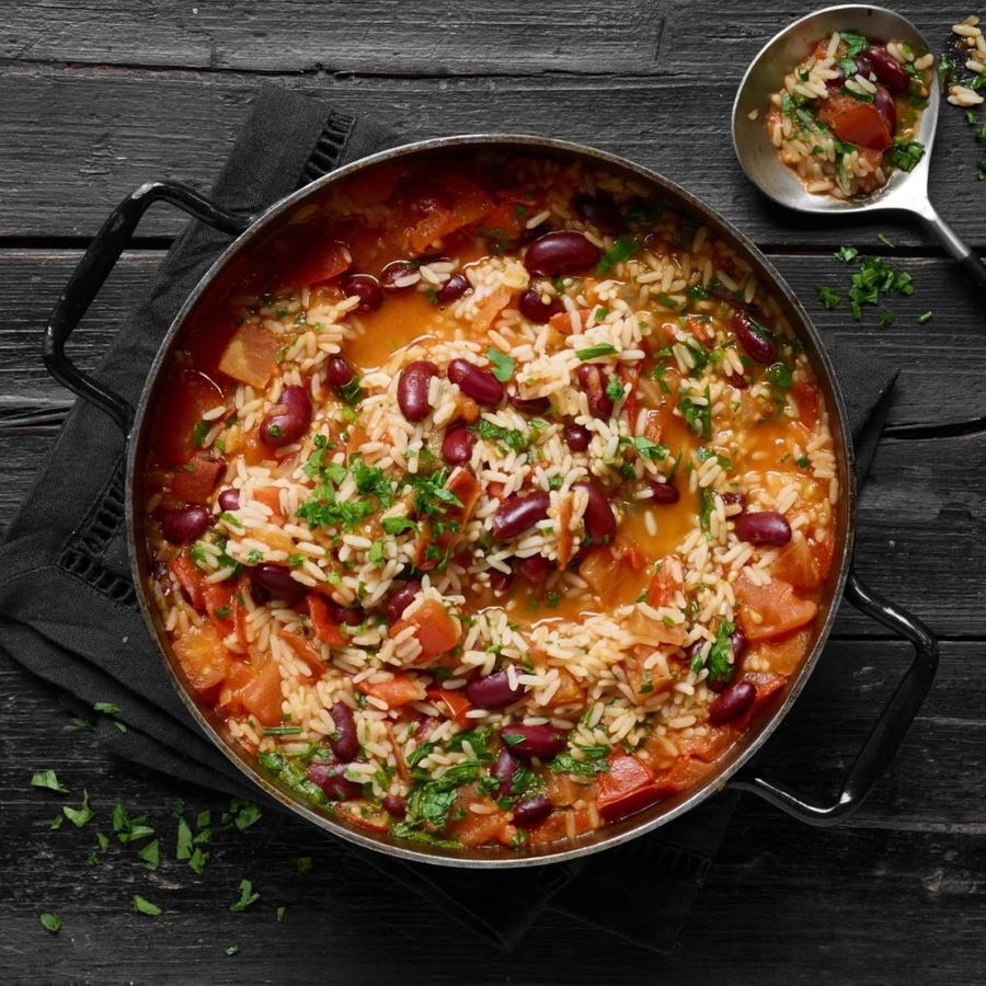 Reisgericht mit Bohnen und Tomaten in einer Pfanne auf einem Holztisch