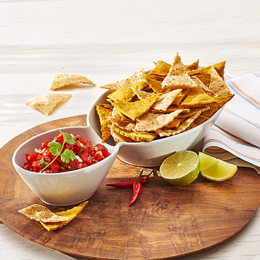 Schüssel mit Tortilla-Chips, Salsa, Limette und Chili auf Holzbrett