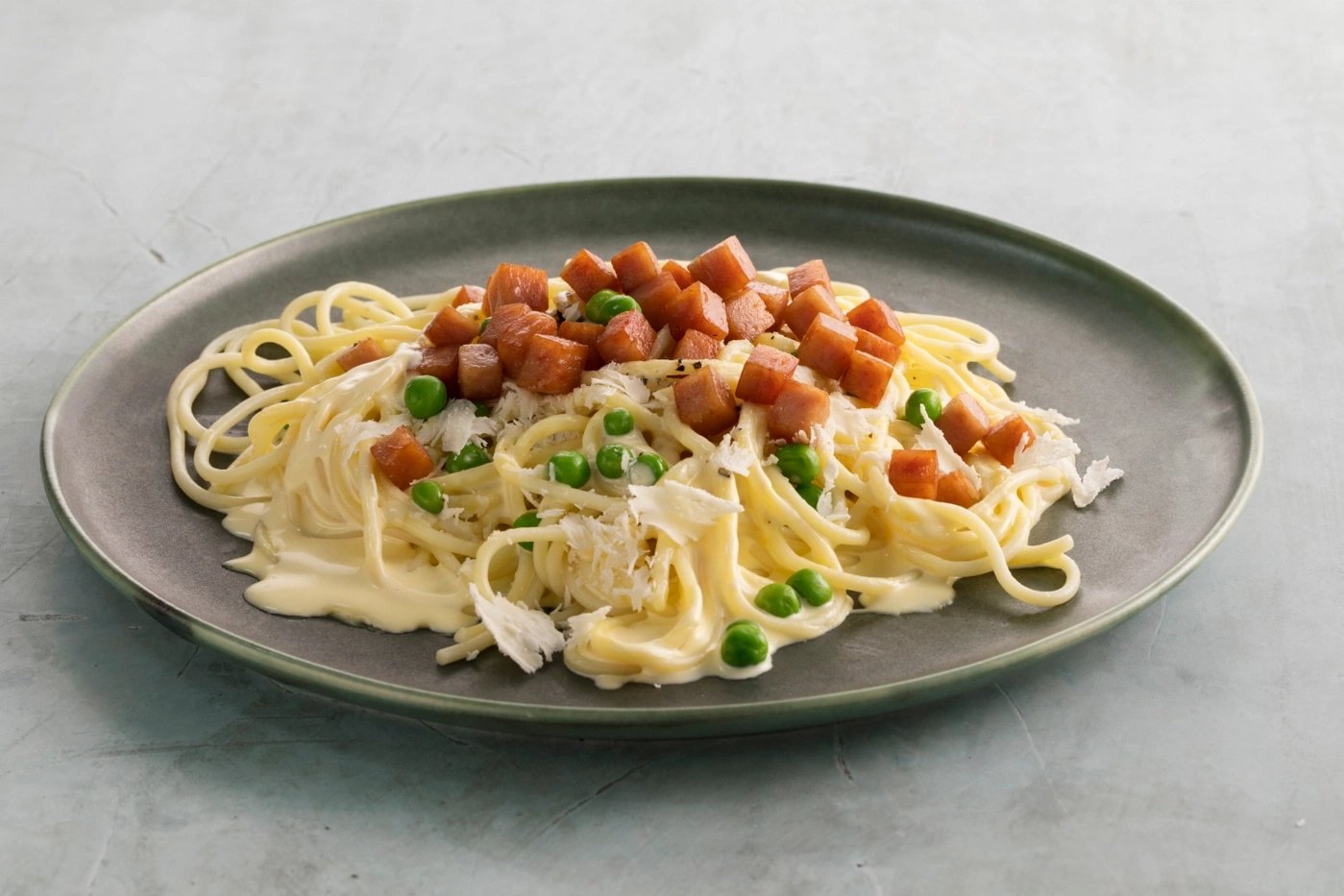 Spaghetti mit Speckwürfeln, Erbsen und Käse auf einem Teller.