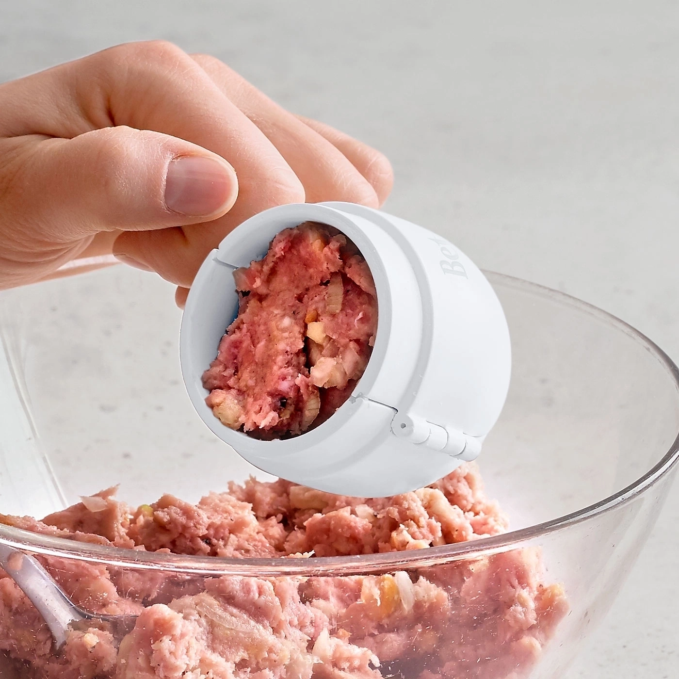 Nahaufnahme von Fleisch in einem Fleischbällchenformer und einer Schüssel.