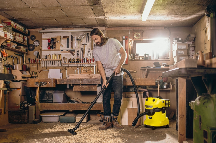 Ein Mann saugt Holzspäne in einer Werkstatt mit einem gelben Kärcher Sauger auf.