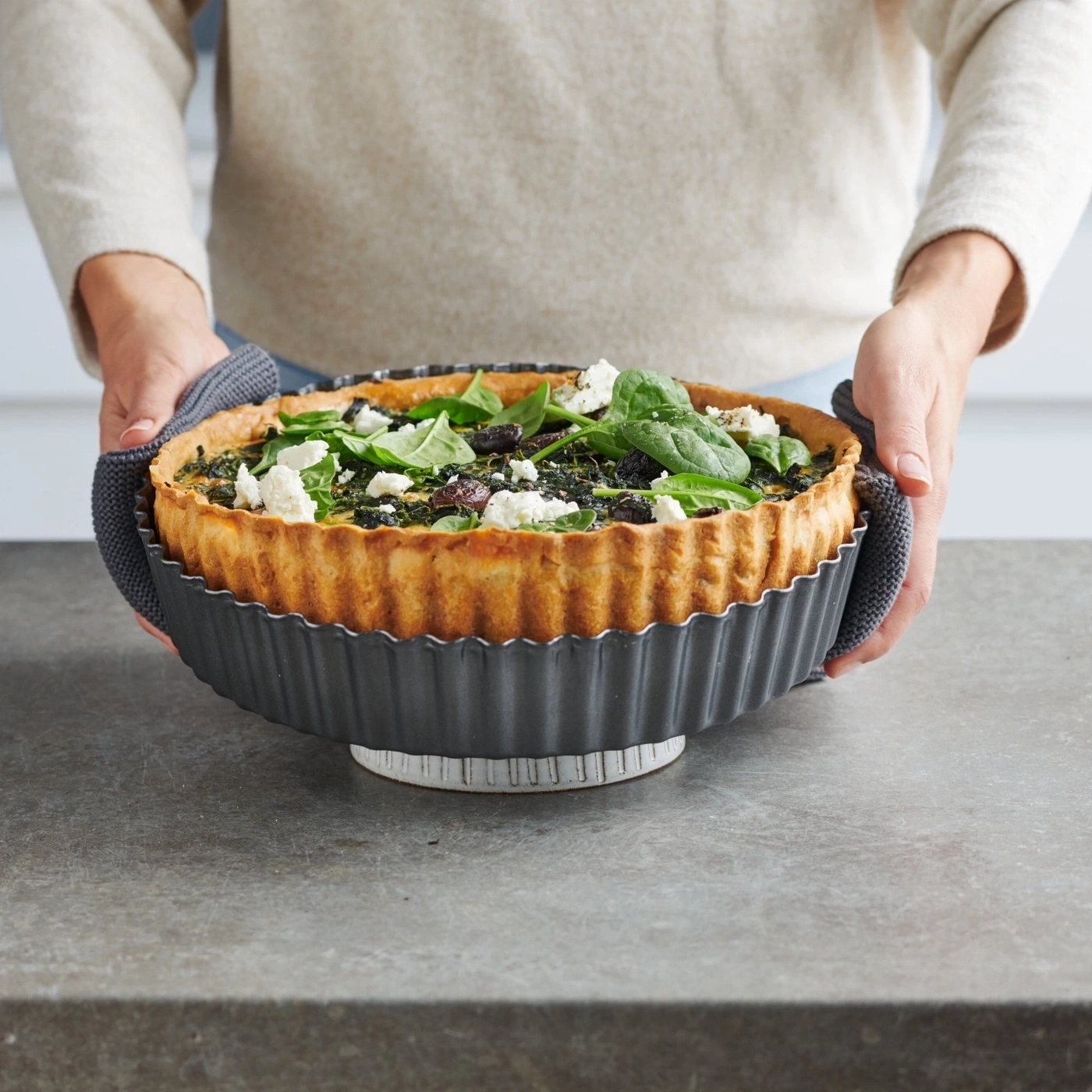 Person hält eine Quiche in einer Kuchenform mit Ofenhandschuhen