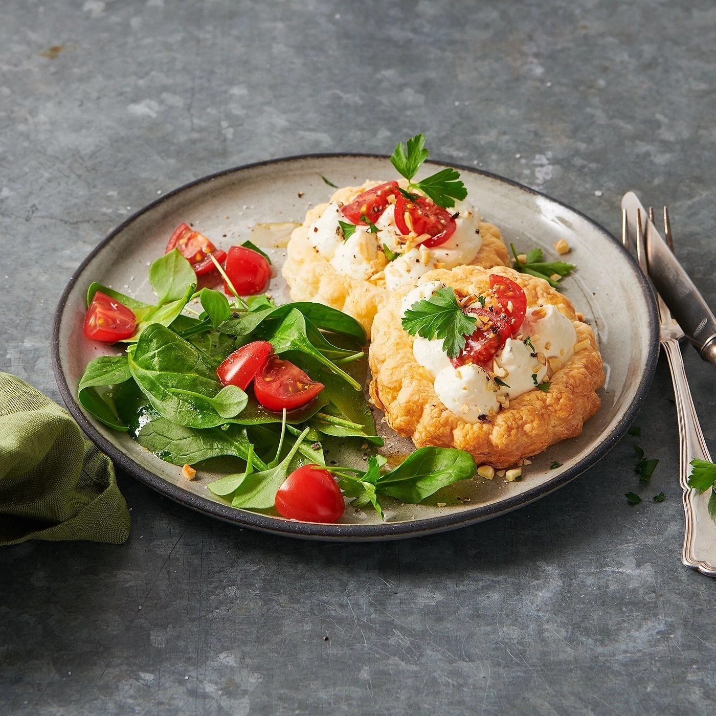 Teller mit Gebäck, Tomaten, Salat und Besteck auf grauem Hintergrund