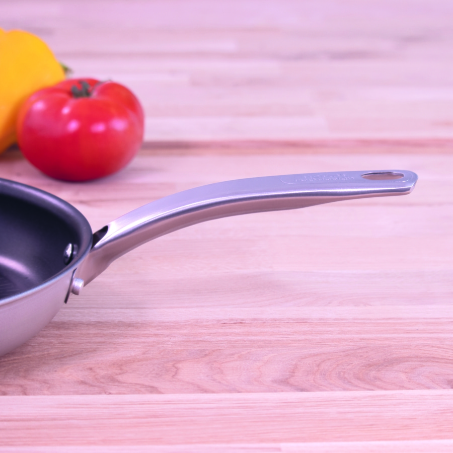 Pfanne mit Griff auf Holzoberfläche, Tomate und Paprika im Hintergrund