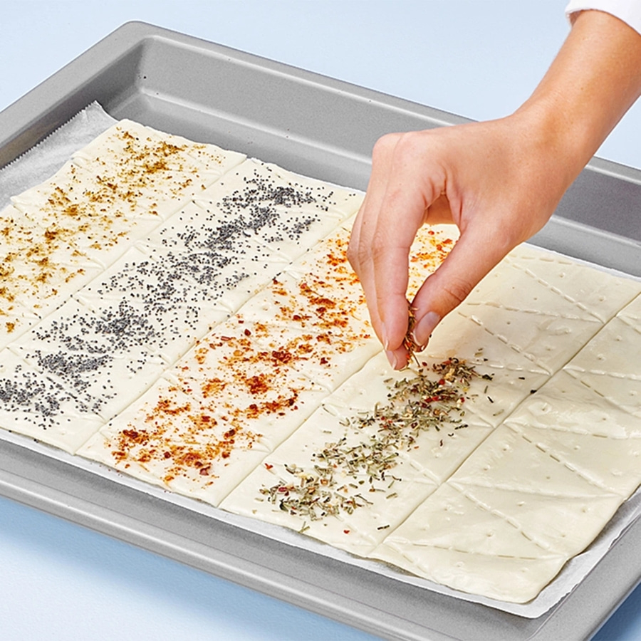 Hand bestreut Gebäck mit Kräutern auf Backblech, Nahaufnahme