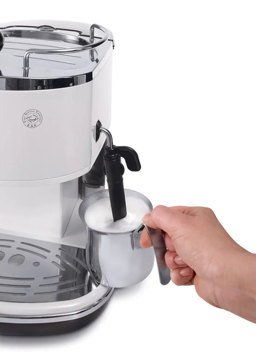 Hand hält Milchkännchen mit aufgeschäumter Milch unter Dampfdüse einer Espressomaschine