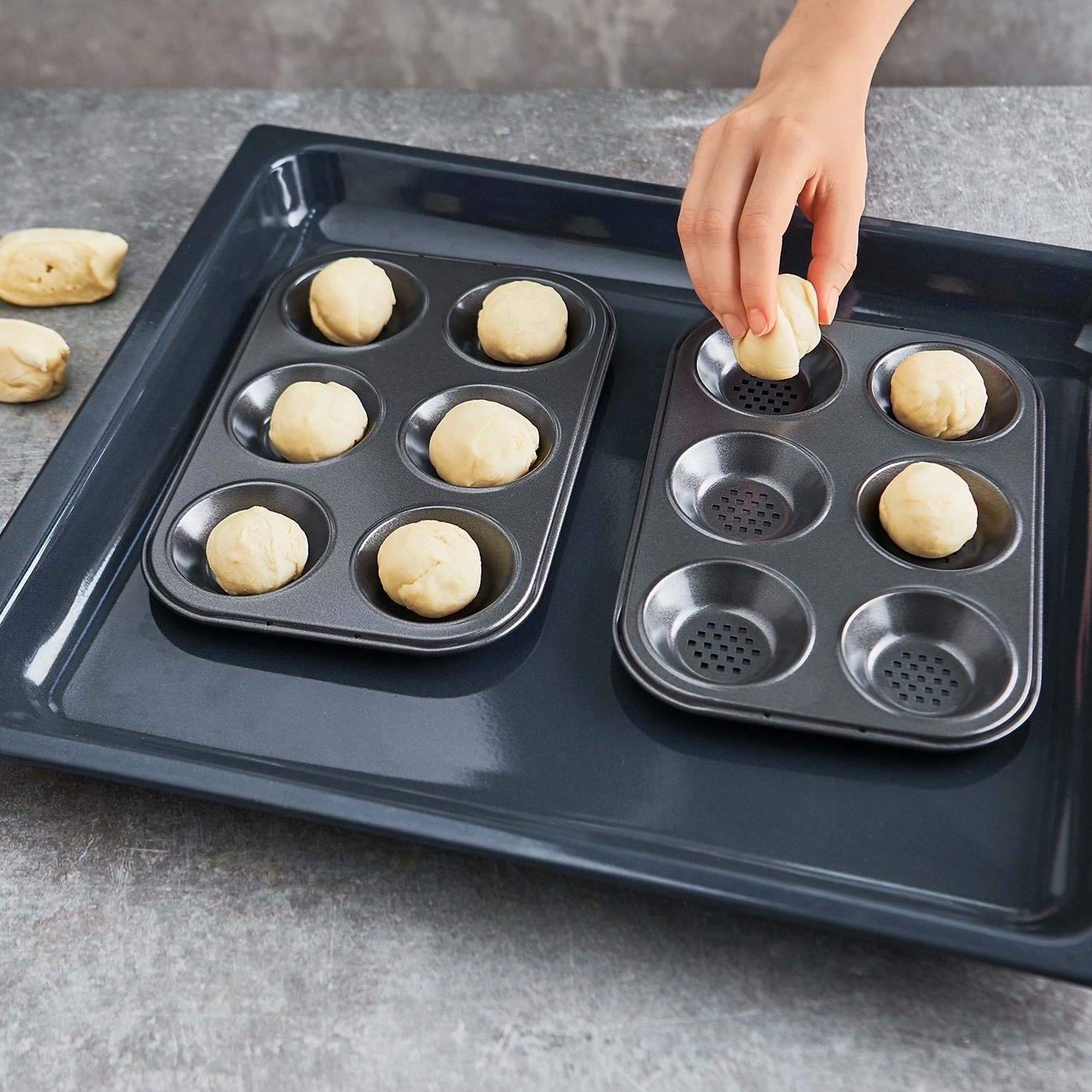Person legt Teigkugeln in Backformen auf einem Backblech. Backen vorbereiten.