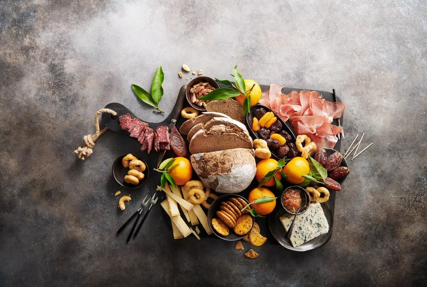 Ein rustikales Brett mit Wurst, Käse, Brot, Früchten und Nüssen.