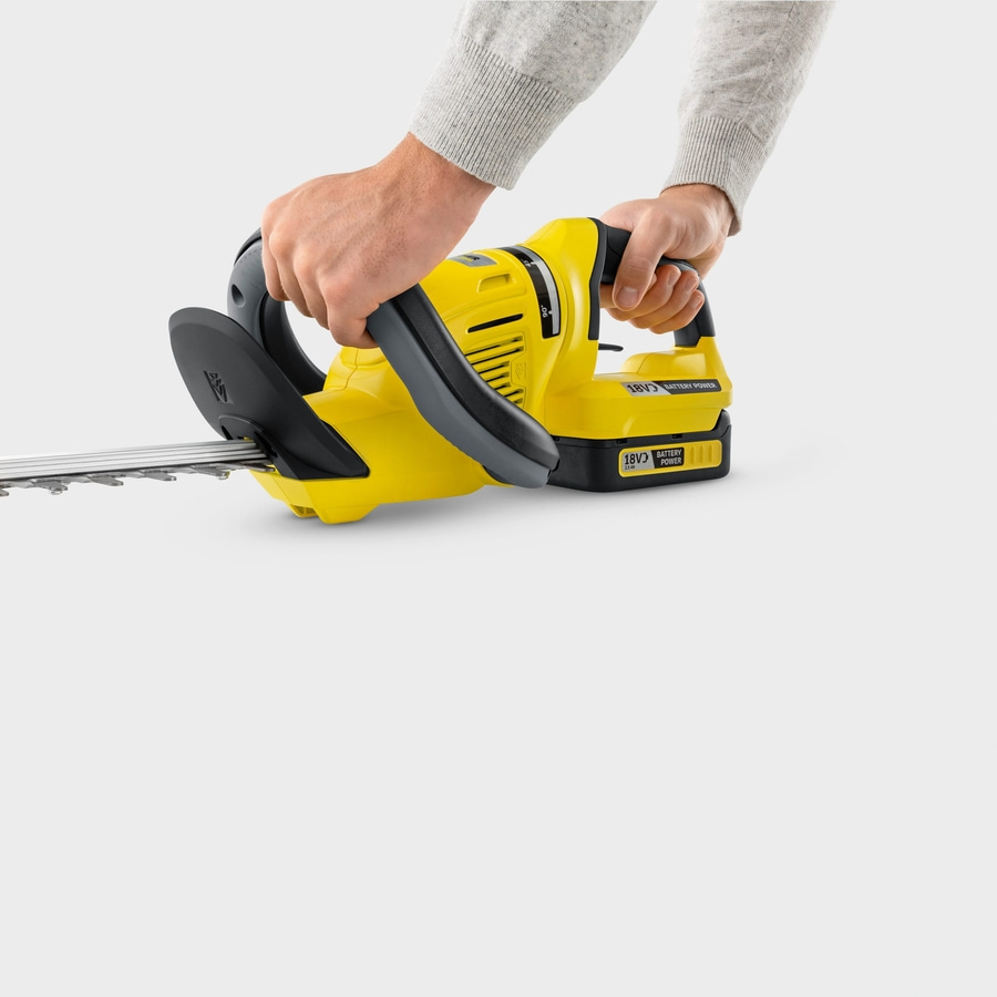 Person hält gelbe Heckenschere mit schwarzen Griffen und grauen Ärmeln