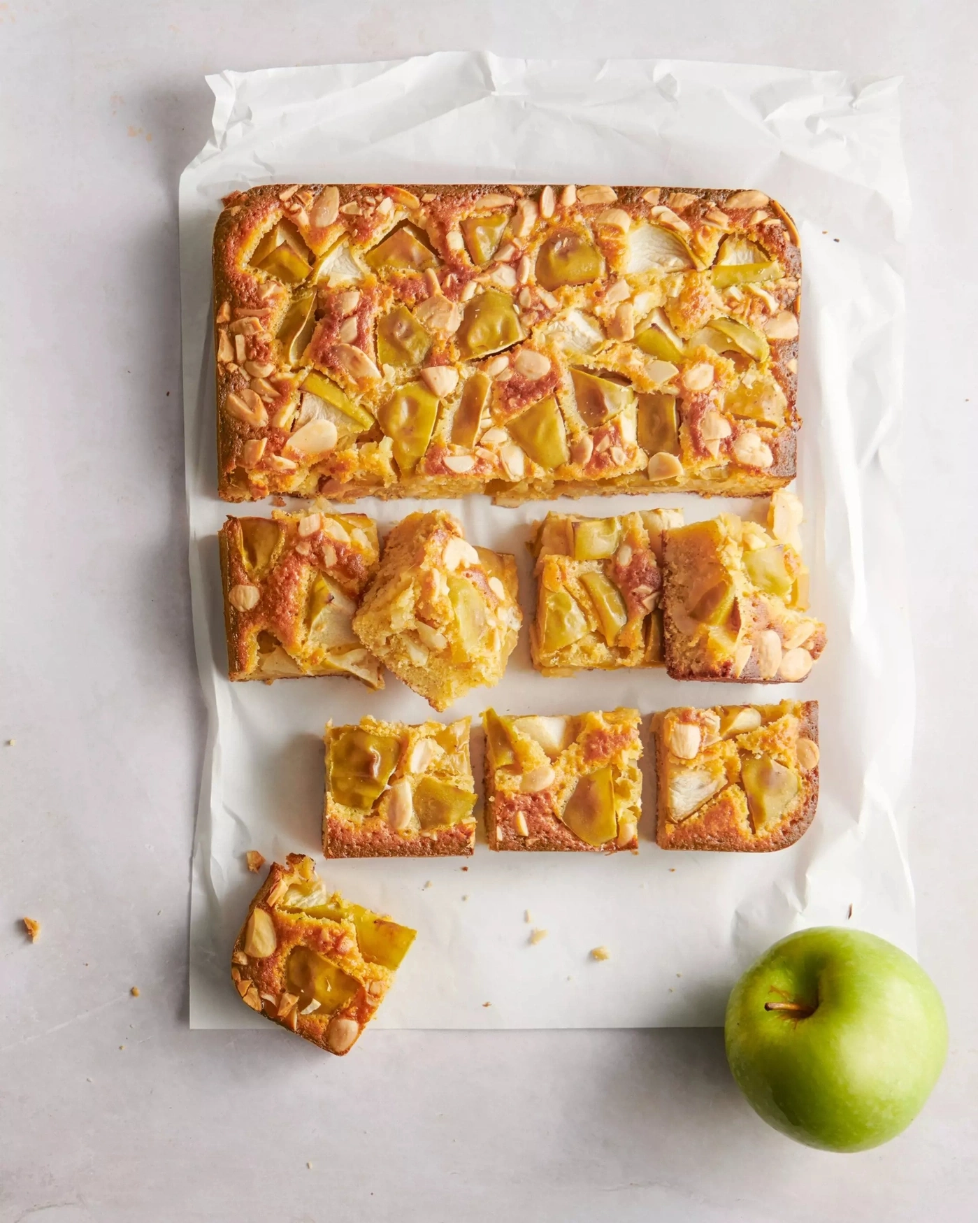 Apfelkuchen mit Mandeln auf Backpapier, angeschnitten