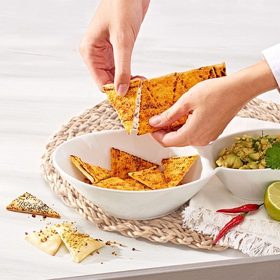 Hände halten Tortilla-Chips über einer Schüssel mit Guacamole und Zutaten.