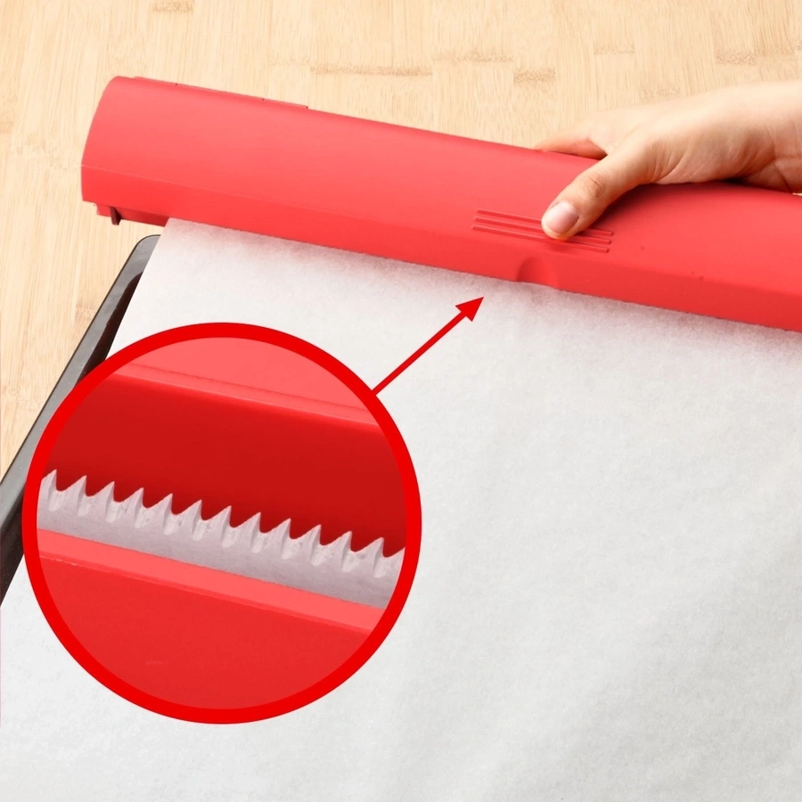 Rotes Küchenwerkzeug schneidet Backpapier. Nahaufnahme der gezahnten Klinge.
