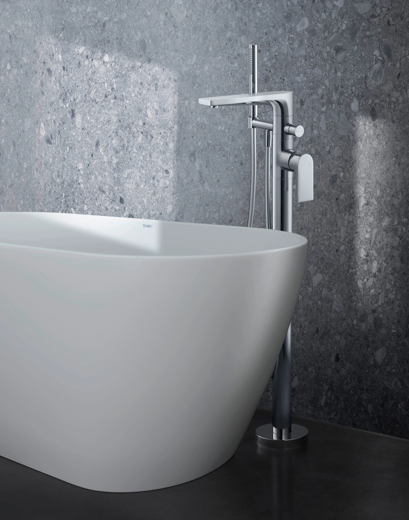 Freistehende Badewanne mit Chromarmatur vor einer grauen Steinwand.