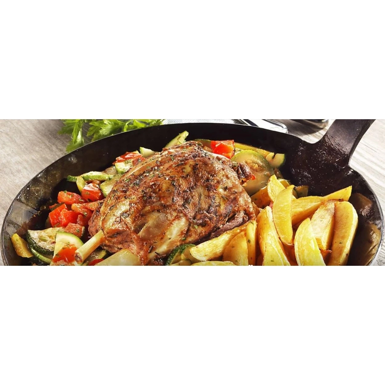 Gegrillter Lammkeule mit Bratkartoffeln und Gemüse in einer Pfanne.