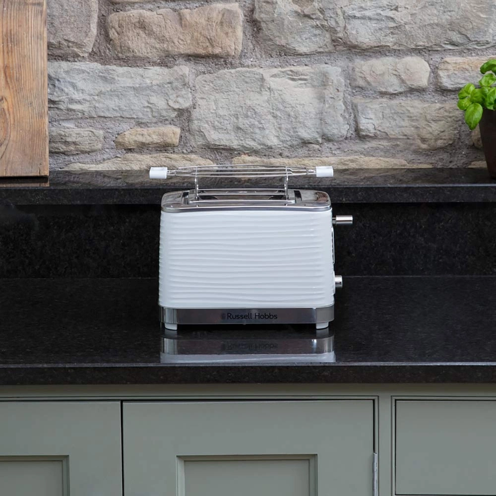 Weißer Toaster von Russell Hobbs auf einer schwarzen Oberfläche vor einer Steinmauer.