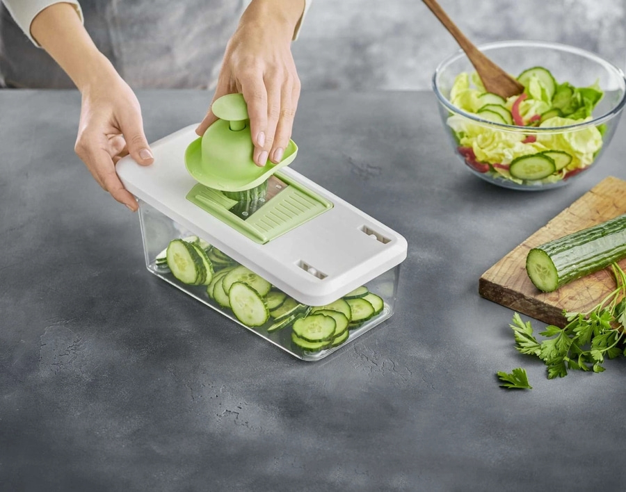 Person schneidet Gurke mit einem Gemüseschneider, Salat in einer Schüssel.