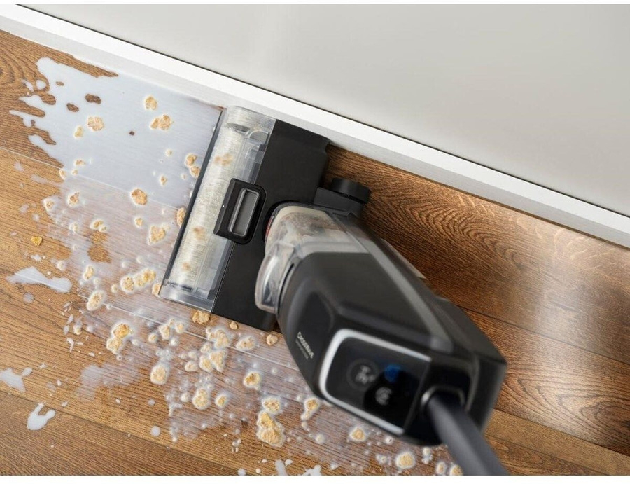 Staubsauger reinigt verschüttete Flüssigkeit und Krümel auf Holzboden an der Wand.