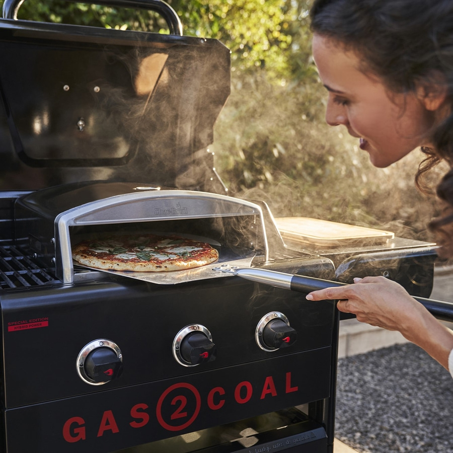 Frau backt Pizza im Grill. Gas 2 Coal Grill. Pizza wird gebacken.